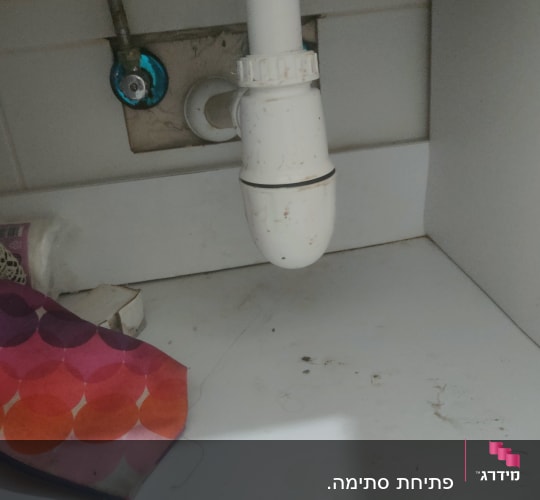 צינור ניקוז לבן מתחת לכיור עם חיבורי מתכת
